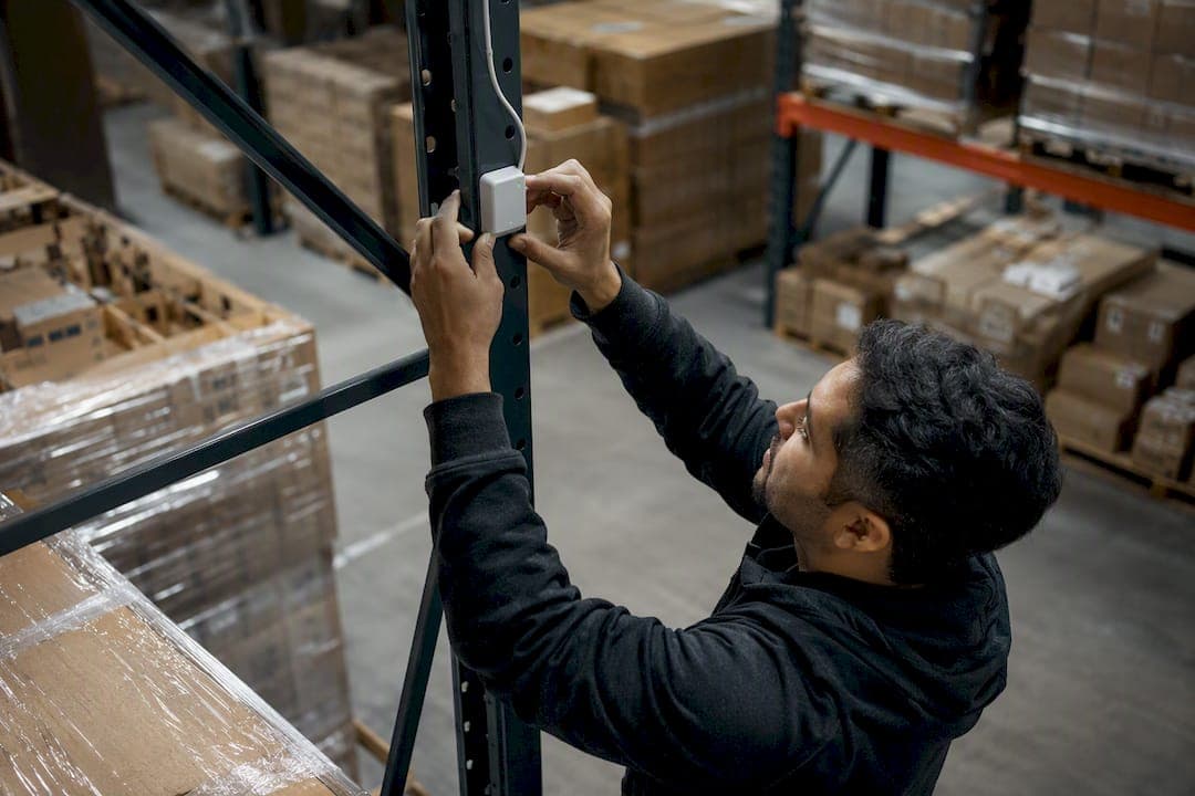 Hands installing sensor in warehouse shelving