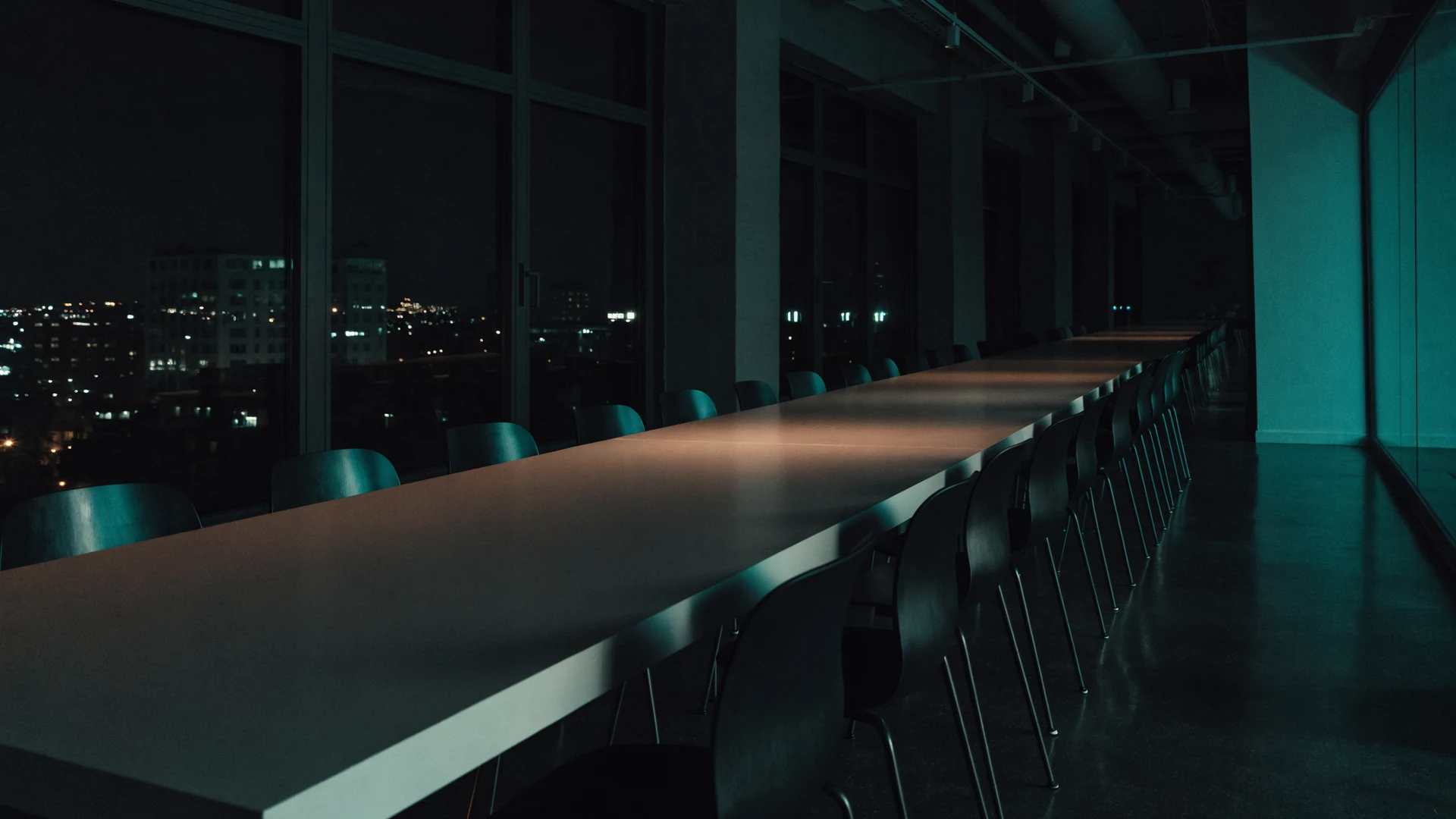 Empty communal loft table at night, chairs waiting along both sides