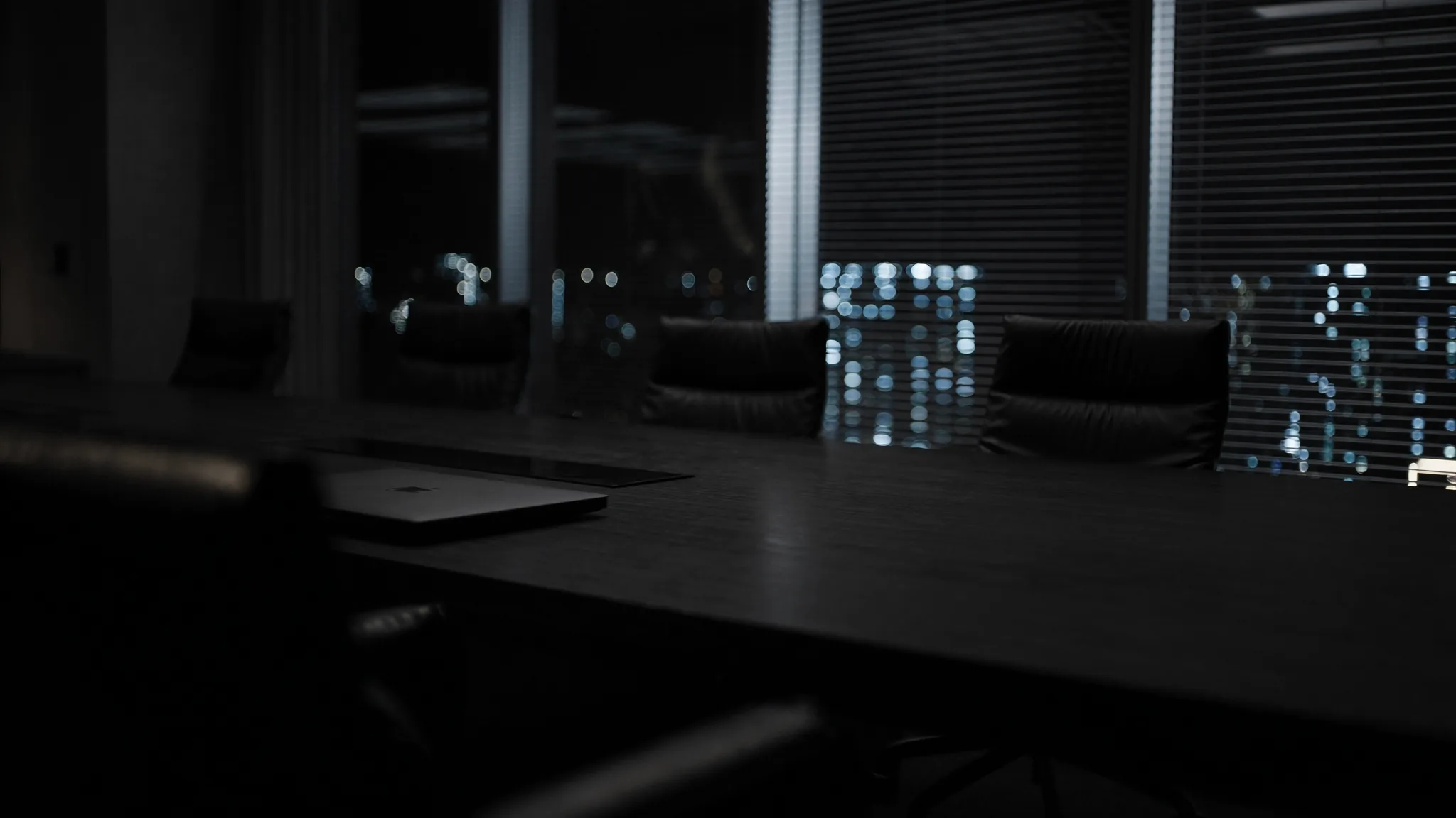 After-hours conference table in a hospitality office, laptop and coffee waiting for a decision that has no owner