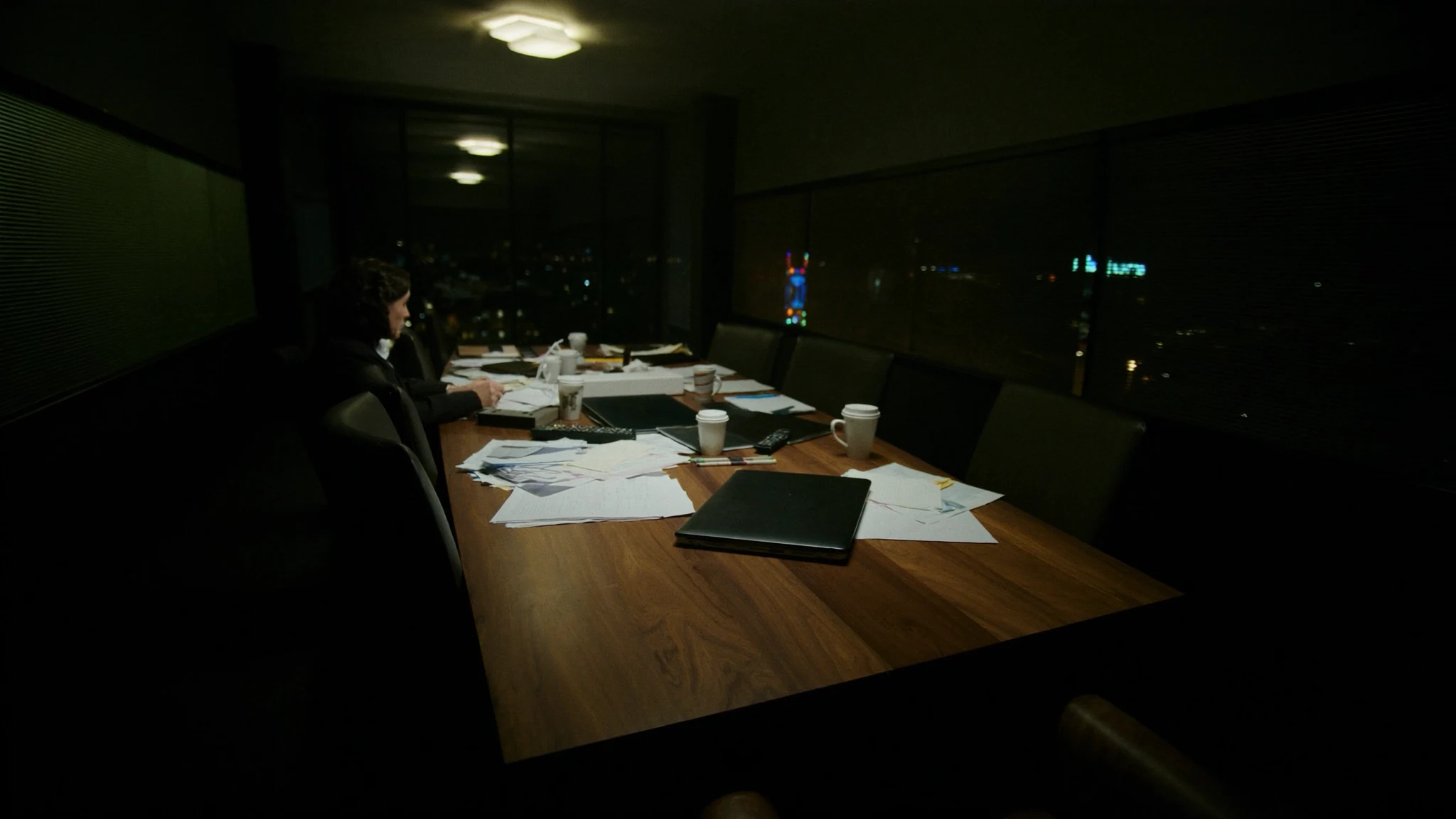 After-hours conference table in a media office, laptop and coffee waiting for a decision that has no owner